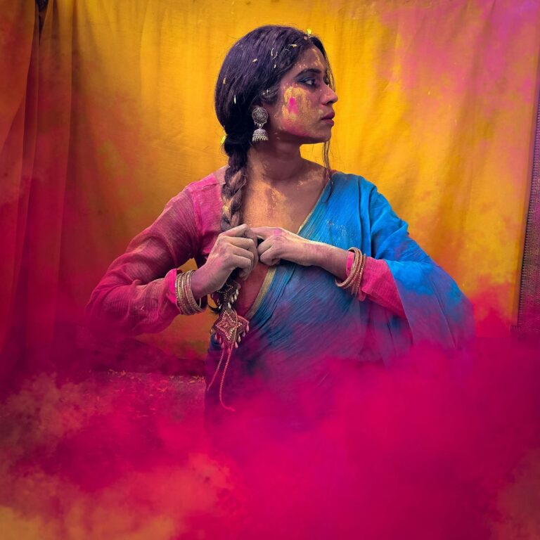 Woman enjoying Holi festival with vivid powder colors on sari and face.