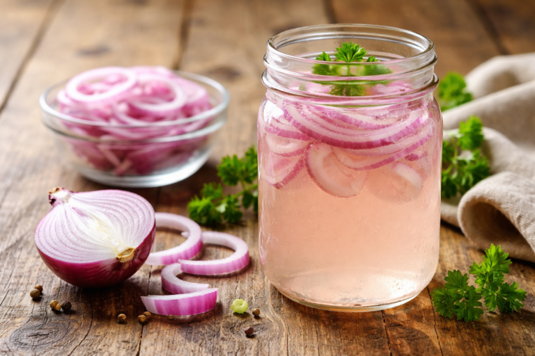 Jar of onion water with sliced red onions on a wooden table, natural remedy for hair growth and bald patches.
