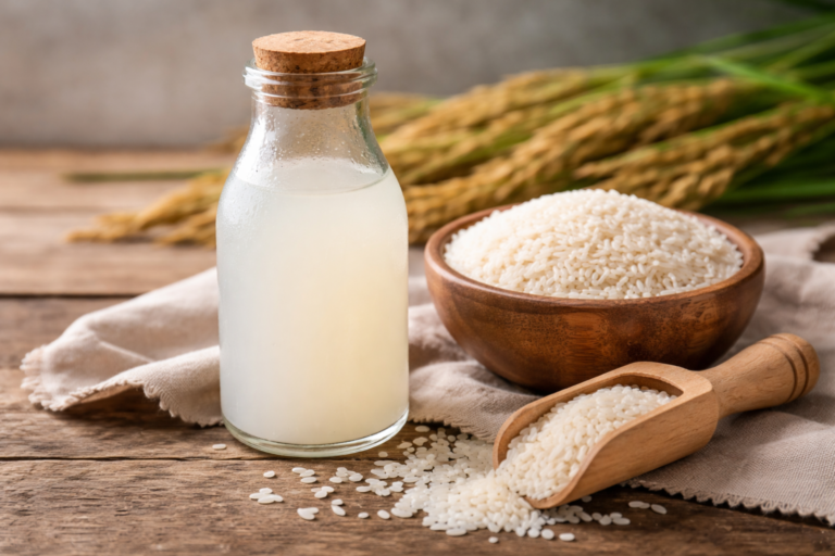 Rice water in a glass bottle with raw rice in a wooden bowl placed on a rustic surface